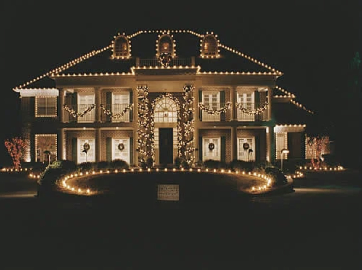 Estate home with warm white roofline and balcony garland holiday lighting